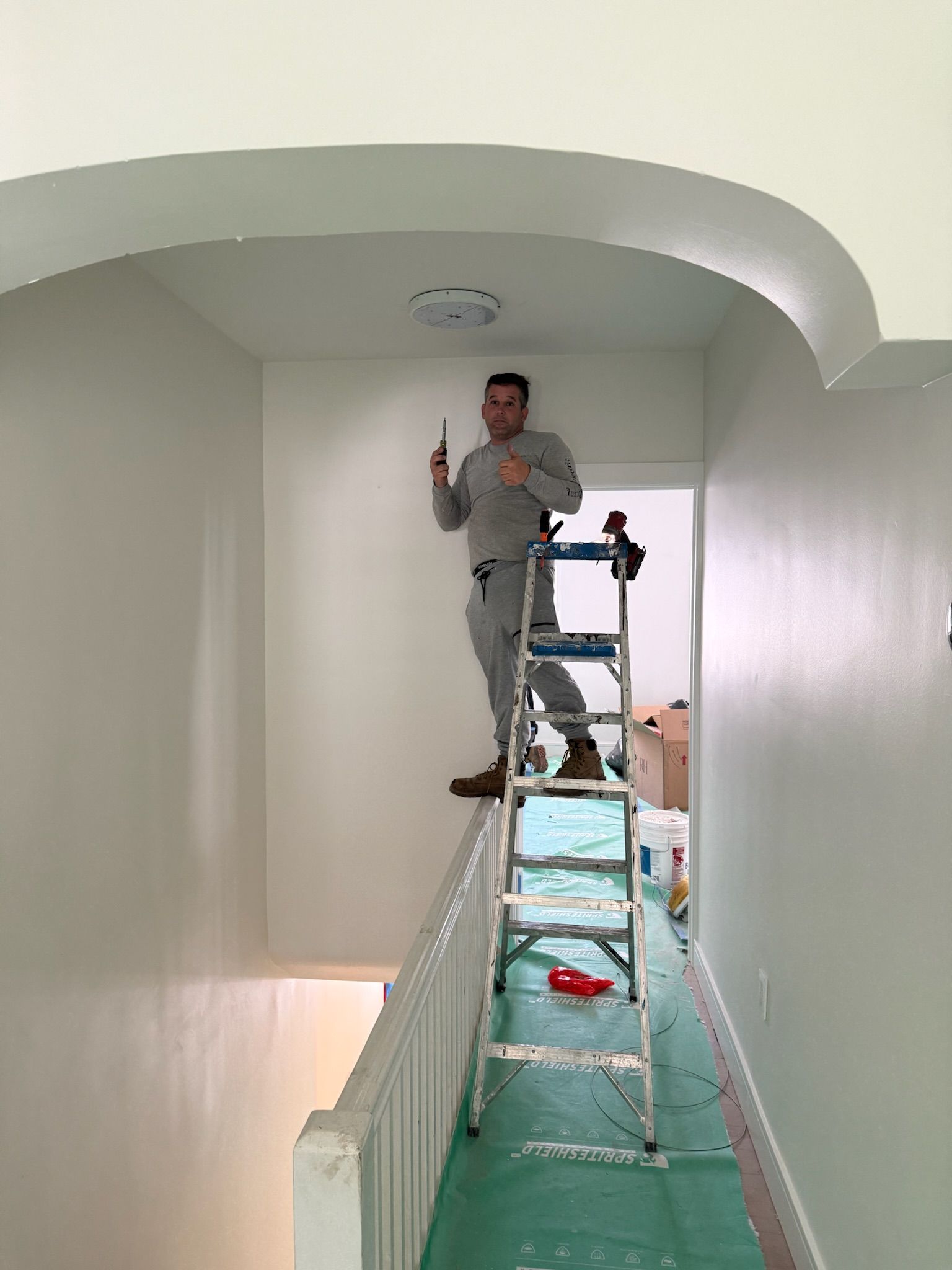 Electrician installing a ceiling device in a hallway