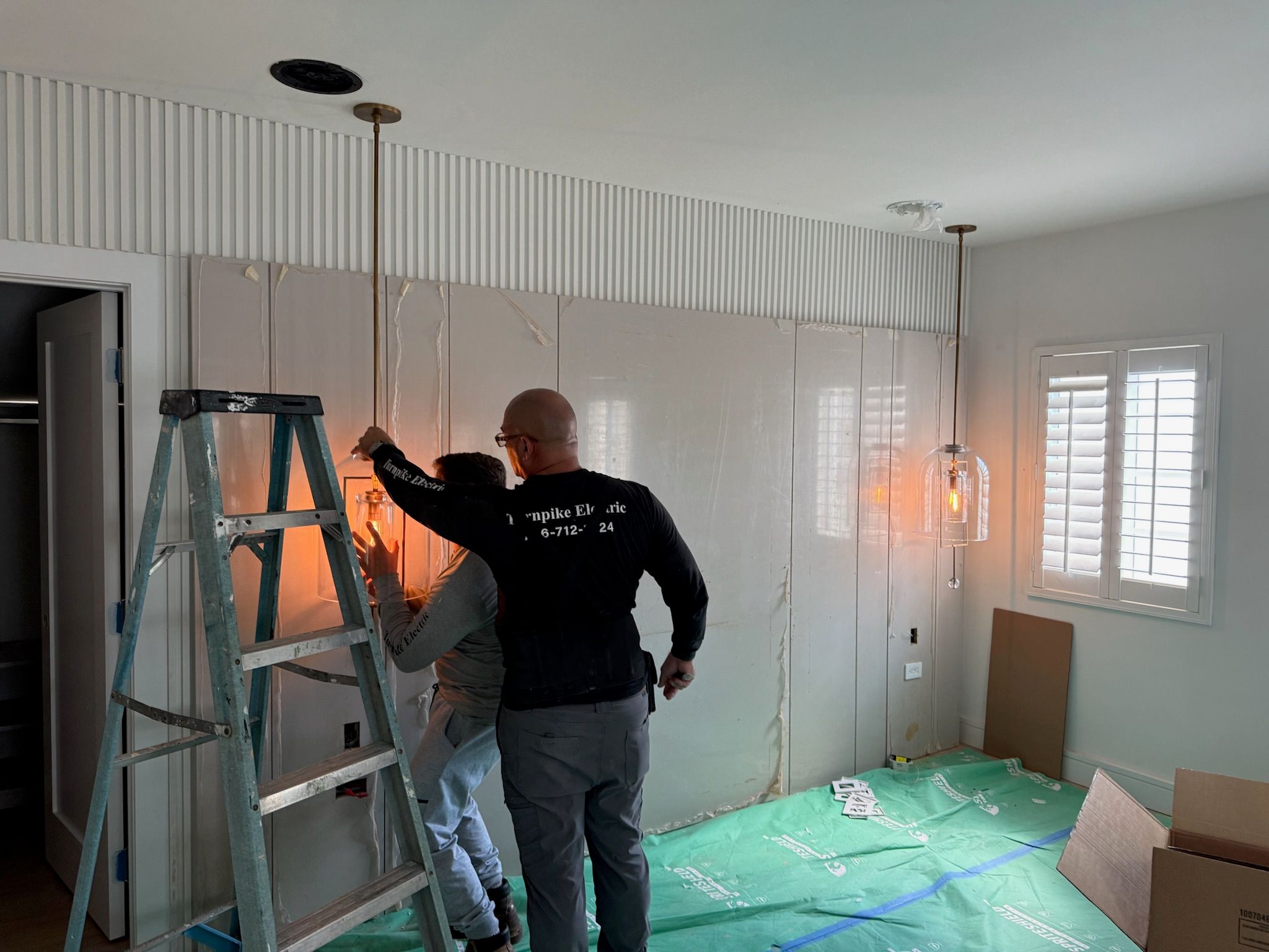 Electricians installing pendant lighting in a finished room